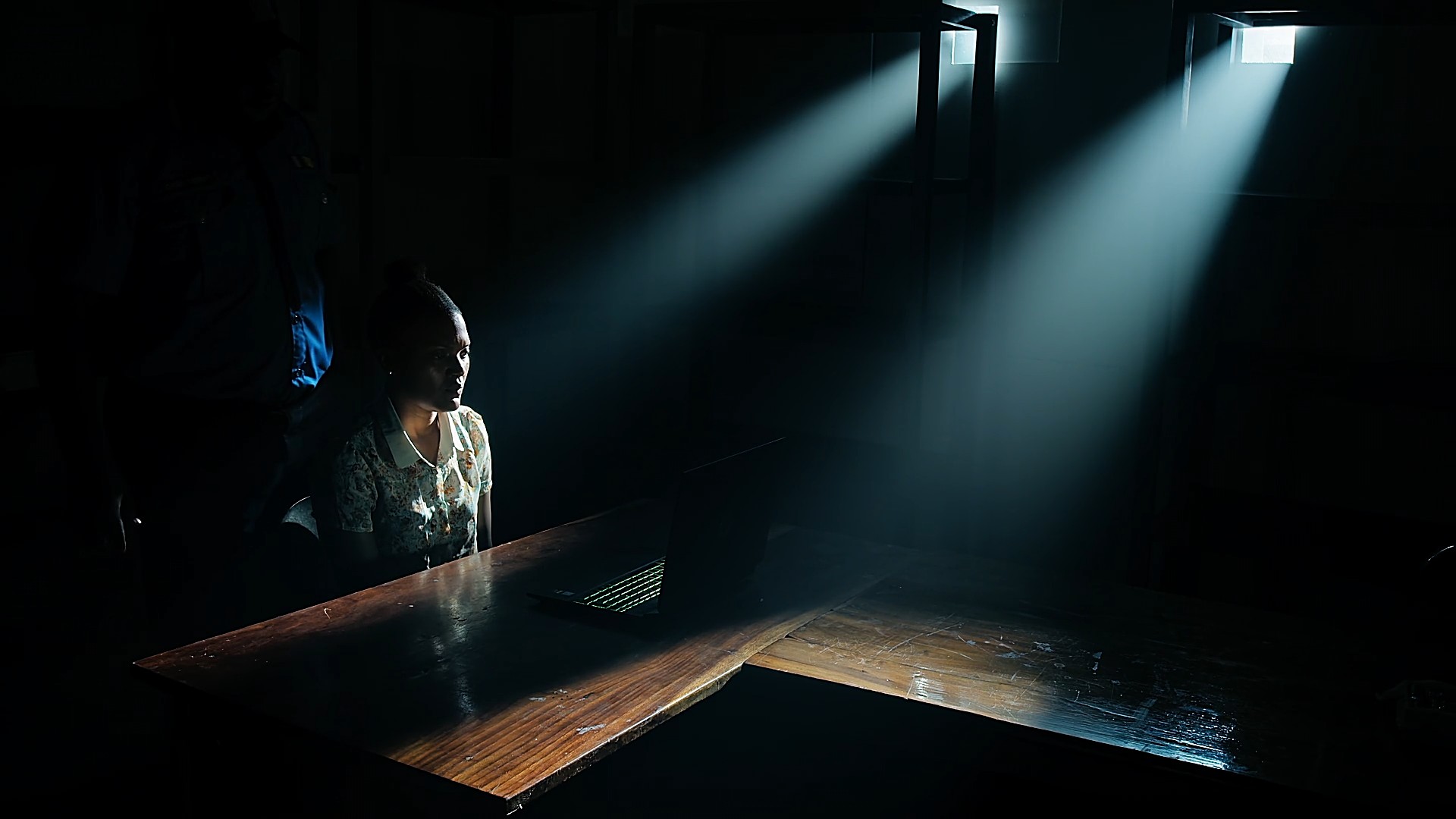A noir film scene, a woman sits in a dark room, the only light coming from two small windows creating god rays.